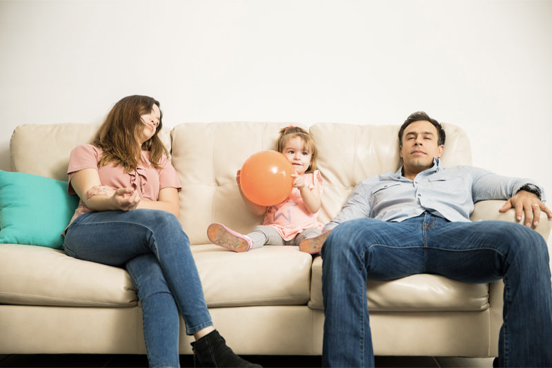 Parenthood and Sexuality, husband and wife exhausted with baby girl sitting between them holding a balloon, happy